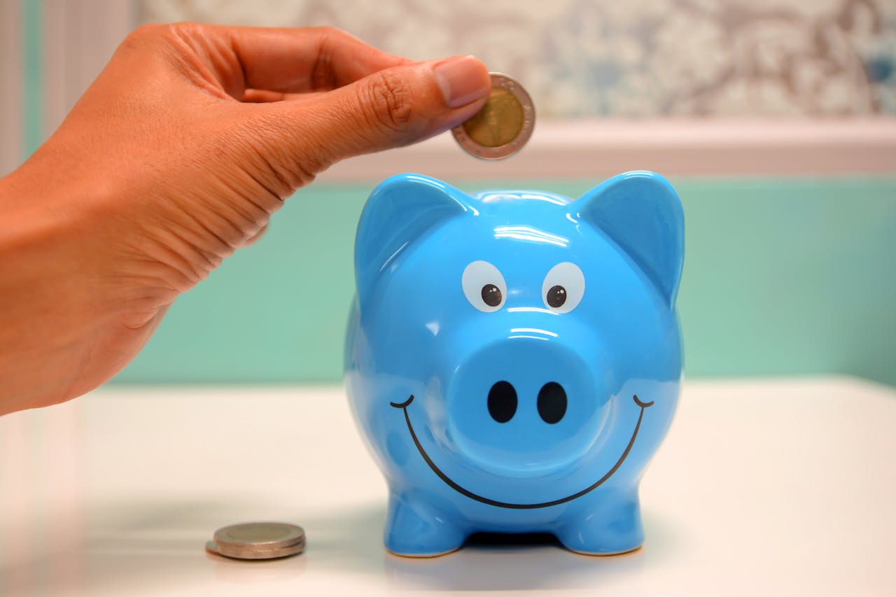 service-02 Hand inserting a coin into a blue piggy bank for savings and money management.